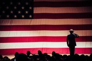 man standing on stage facing an american flag, strip club, free admission